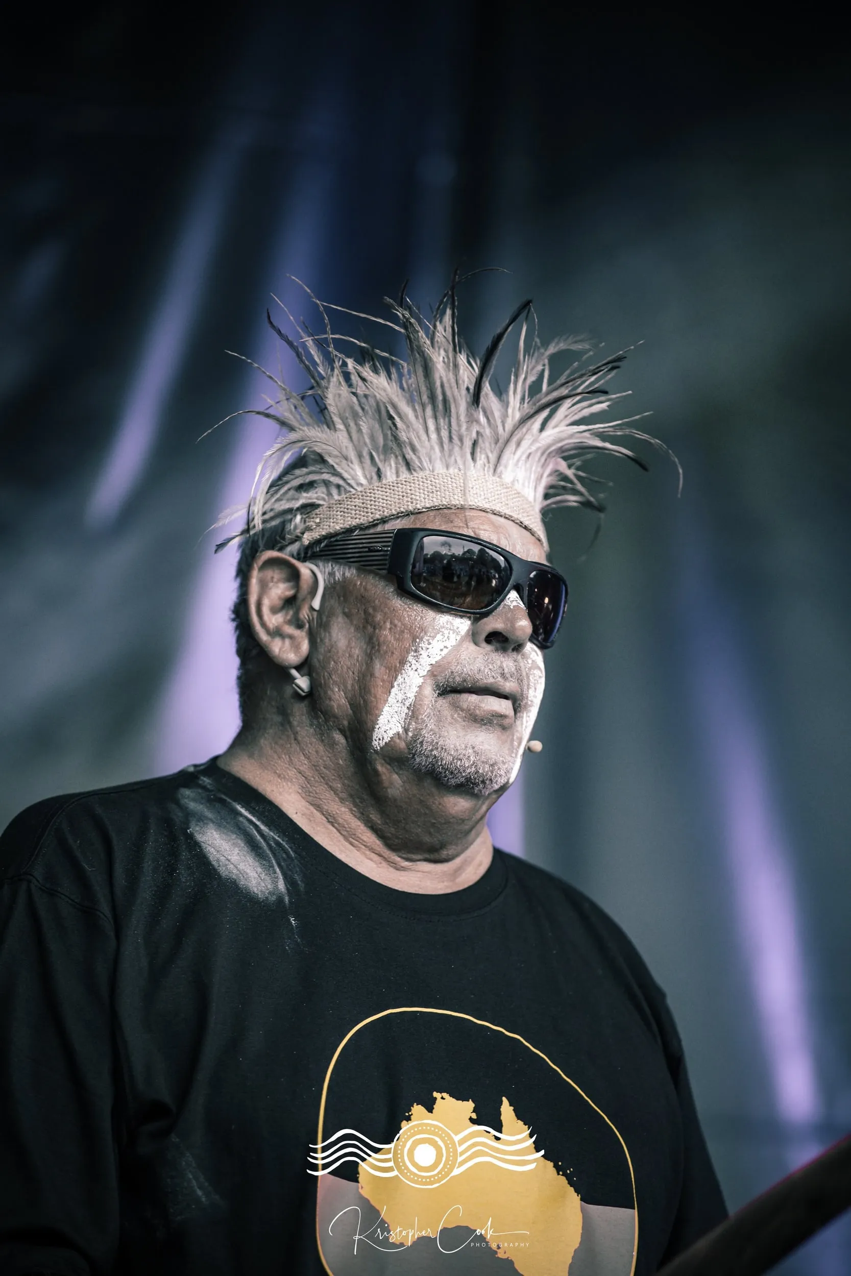 Elder in sunglasses and ochre on stage at Groove on the Grass, Grafton, 2023, photographed by Kris Cook